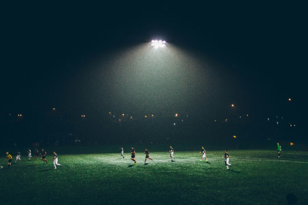 abigail-keenan-8-s5QuUBtyM-unsplash Soccer players playing under stadium lights during an evening football game